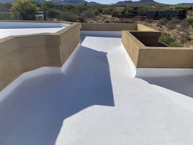 Workers applying a white coating to a flat roof with parapet walls, showing a maintenance process.