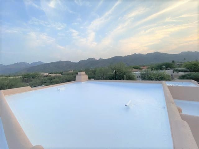 Flat white roof with parapet walls and a vent, showing a well-maintained roofing surface under a partly cloudy sky with mountains and trees in the background.